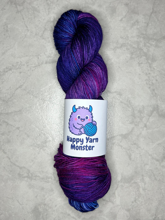 1 skein of hand-dyed yarn, on the Sock Monster base. In the colorway Fairy Night, which have variegated pink, blue en purples. The skein has a "Happy Yarn Monster" label.