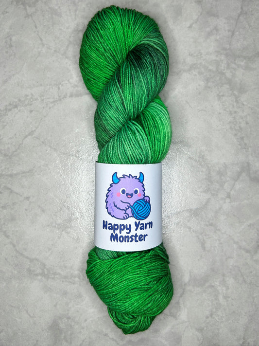 1 skein of hand-dyed yarn, on the Sock Monster base. In the colorway Forest Stroll, which has a green variegated base with darker and lighter greens. The skein has a "Happy Yarn Monster" label.