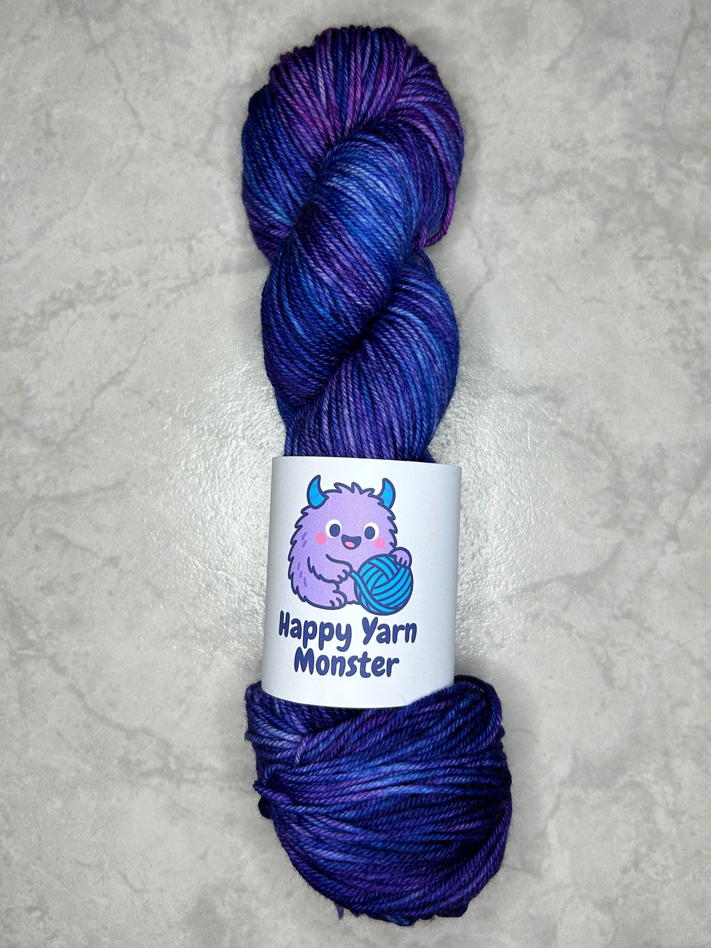 1 skein of hand-dyed yarn, on the DK Sock Monster base. In the colorway Fairy Night, which have variegated pink, blue en purples. The skein has a "Happy Yarn Monster" label.